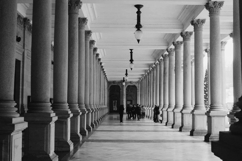 The colonnade of an institutional building, columns receding in perspective with figures in the distance.
